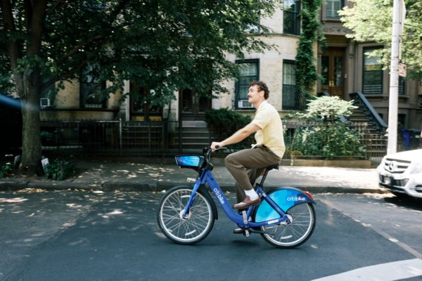Мужчина едет на синем велосипеде Citi Bike по улице вдоль домов и деревьев